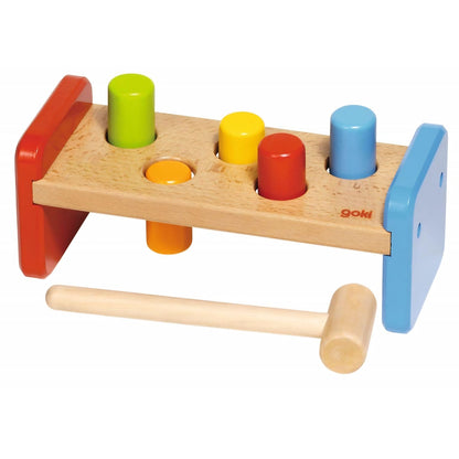 Brinquedo de madeira Goki com martelo e elementos coloridos no banco.
