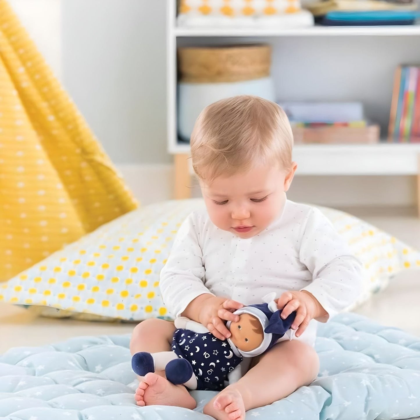 Bebé com Boneca Pano Azul com Vestido Estrelado da Corolle em ambiente de brincadeira suave