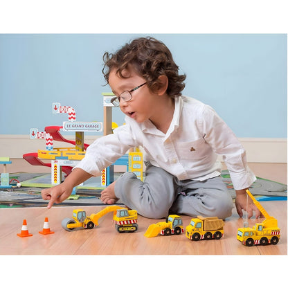 Criança a brincar com veículos de construção em madeira Le Toy Van, incluindo camião, grua, escavadora, pá e cones.