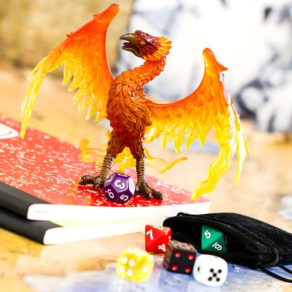Figura de borracha Fénix sobre um caderno, junto a dados de jogo