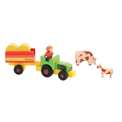 Agricultor no trator verde a puxar o atrelado com fardos, junto a vacas