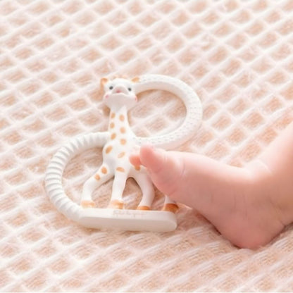 Anel de dentição So Pure Girafa Sofia sobre manta junto ao pé de um bebé
