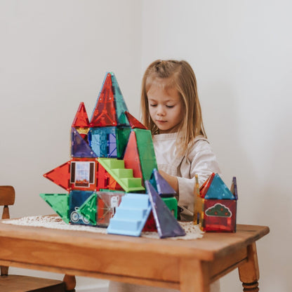 Menina a construir uma casa com Magna-Tiles numa mesa de madeira