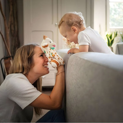 Mãe a brincar com o bebé com o Doudou Marioneta Girafa Sofia junto a um sofá