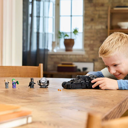 Rapaz a brincar com o LEGO Batman Tumbler numa mesa de madeira