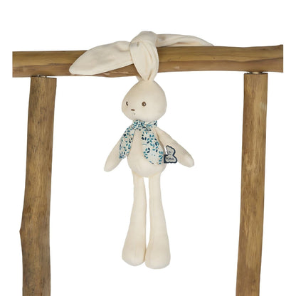 Peluche Coelho Creme 25 cm da Kaloo pendurado pelas orelhas numa barra de madeira
