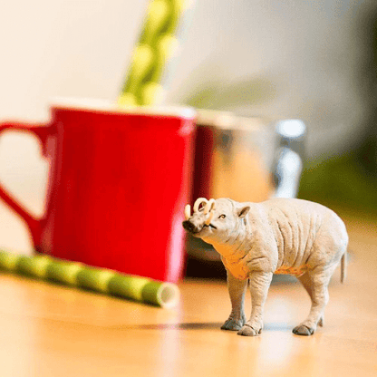 Figura de borracha Babirussa numa mesa junto a uma caneca vermelha
