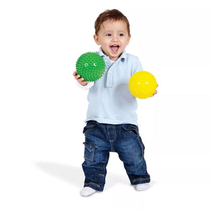 Menino de pé a segurar a Bola Sensorial Verde e uma bola amarela