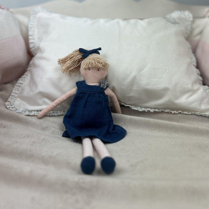 Boneca com Vestido Azul sentada junto a uma almofada branca