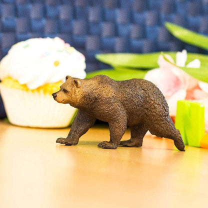 Figura de borracha Urso Pardo numa mesa junto a um queque com cobertura