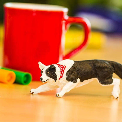 Figura de borracha Border Collie numa mesa junto a uma caneca vermelha