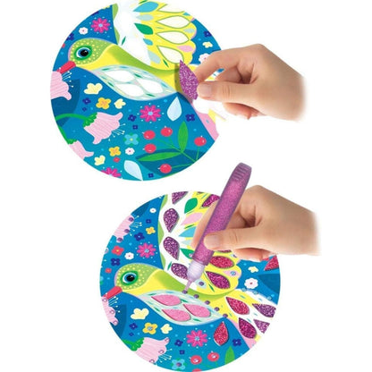 Mão decora um cartão de Pássaros Cintilantes com caneta de purpurina