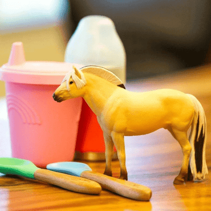 Figura de borracha Cavalo Fiorde sobre uma mesa junto a um copo de criança