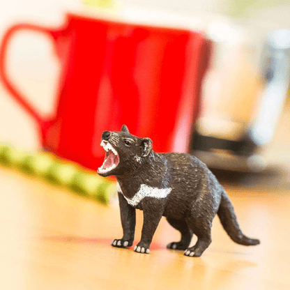 Figura de borracha Diabo-da-tasmânia numa mesa junto a uma caneca vermelha