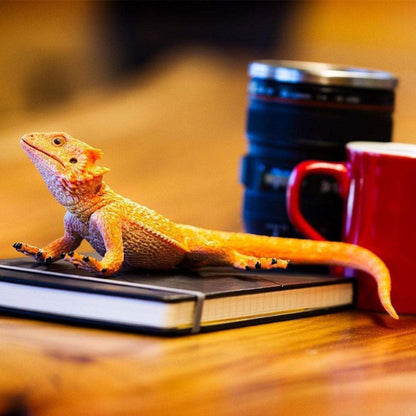 Figura de borracha Dragão Barbudo sobre um caderno junto a uma caneca vermelha