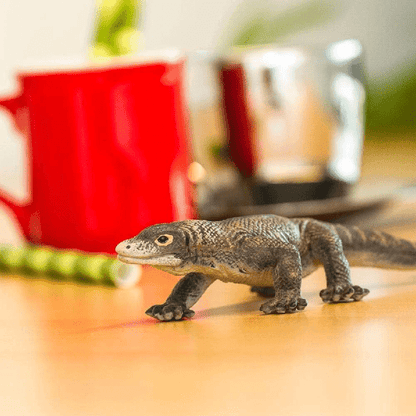 Figura de borracha Dragão de Komodo numa mesa junto a uma caneca vermelha