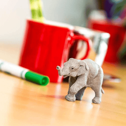 Figura de borracha Elefante Asiático bebé sobre uma mesa junto a uma caneca vermelha