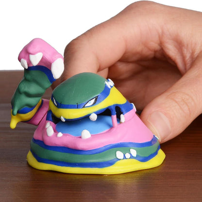 Mão a segurar a figura Pokémon Alolan Muk numa mesa