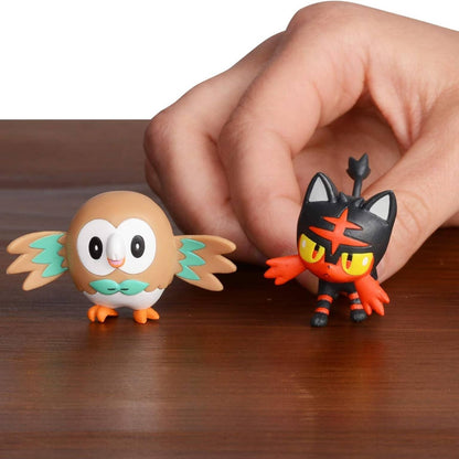 Mão a colocar as figuras Pokémon Rowlet e Litten numa mesa