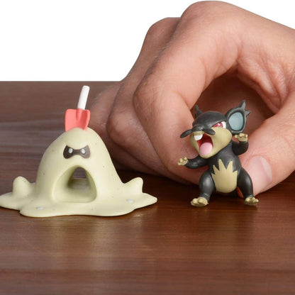 Figuras Pokémon Sandygast e Alolan Rattata sobre uma mesa de madeira