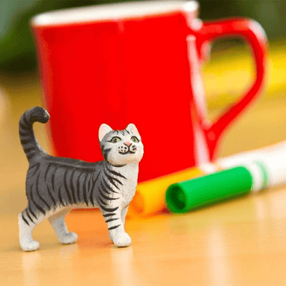 Figura de borracha Gato doméstico cinzento junto a uma caneca e marcadores