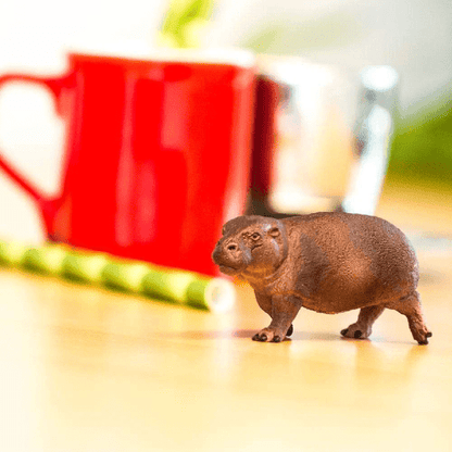 Figura de borracha Hipopótamo Pigmeu numa mesa junto a uma caneca