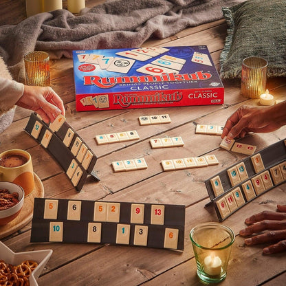 Jogo Rummikub Original em uso numa mesa de madeira, com jogadores a formar sequências de peças