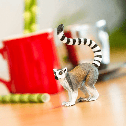 Figura de borracha Lémure de cauda anelada numa mesa junto a uma caneca vermelha