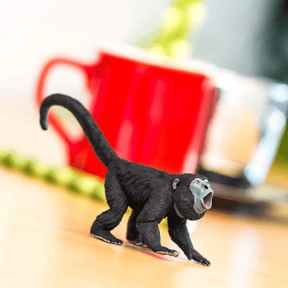 Figura de borracha Macaco Uivador numa mesa de madeira, com caneca vermelha ao fundo