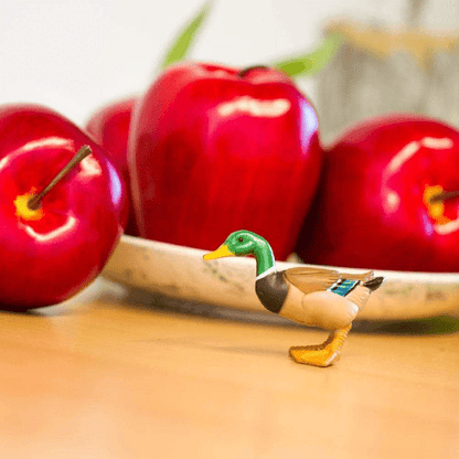 Figura de borracha Pato junto a uma taça com maçãs vermelhas