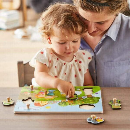 Criança pequena a montar o Puzzle de Pegas O Pomar com a ajuda da mãe