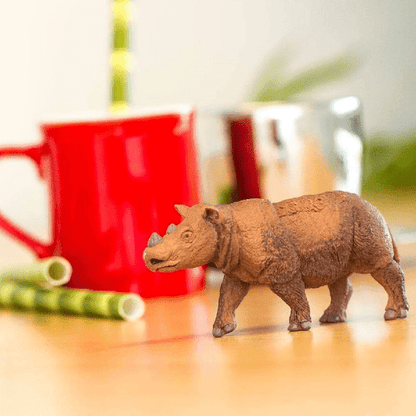 Figura de borracha Rinoceronte da Sumatra numa mesa junto a uma caneca