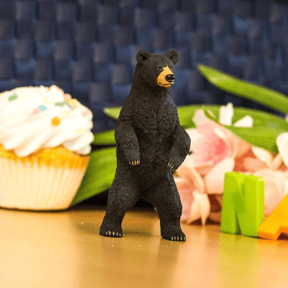 Figura de borracha Urso Negro em pé numa mesa junto a um queque